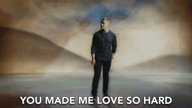 a man in a black shirt is standing in front of a cloudy sky with the words " you made me love so hard " above him