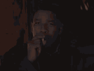 a young man is smoking a cigarette in a dark room with a cigarette in his mouth .