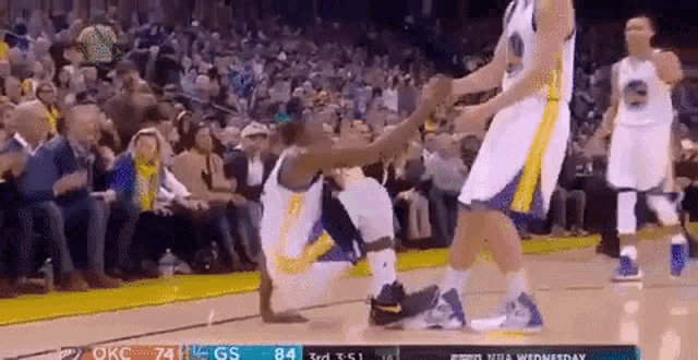 a basketball player is kneeling on the court while another player holds his hand over his knee .