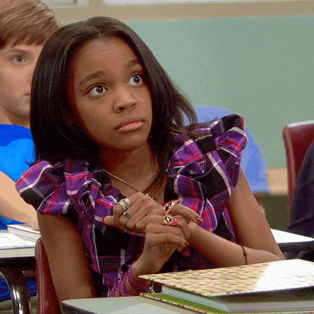 a girl wearing a purple plaid shirt sits at a desk