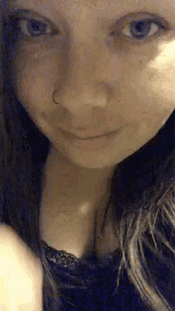 a close up of a woman 's face with a nose ring and a black top .