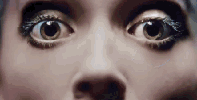 a close up of a woman 's eyes looking at the camera with a surprised look on her face .