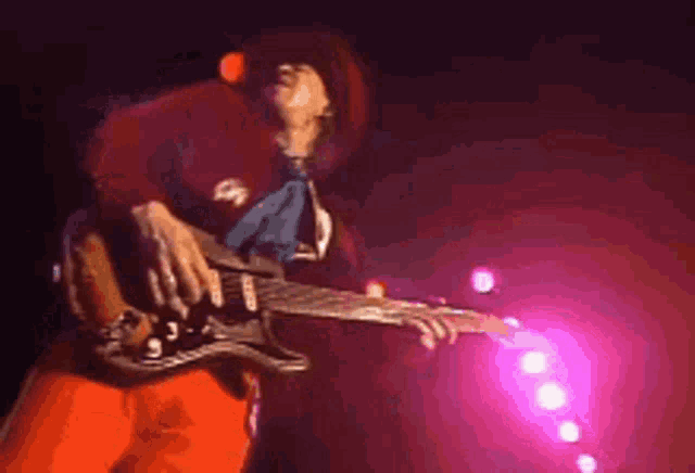 a man in a red hat and red pants is playing a guitar on stage .
