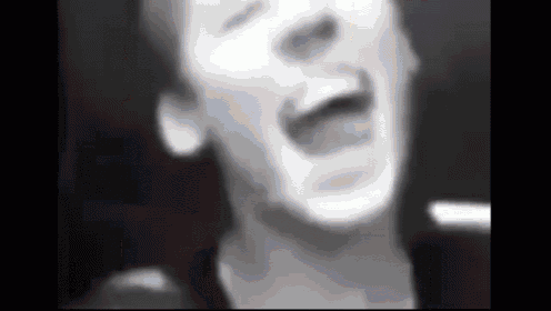 a black and white photo of a man singing into a microphone in a dark room .