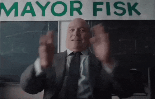a man in a suit and tie stands in front of a mayor fisk sign