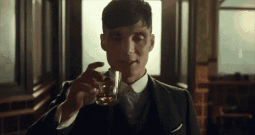 a man in a suit and tie is holding a glass of whiskey .