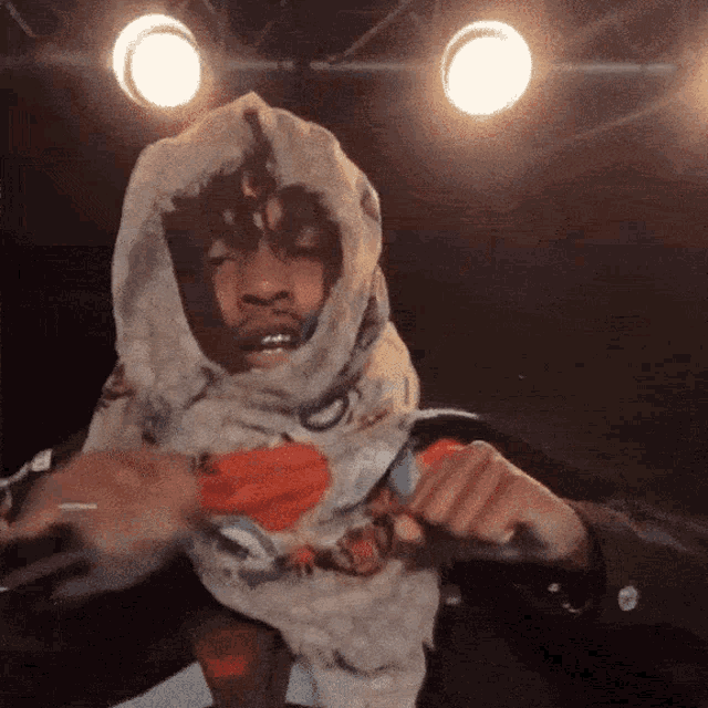 a man wearing a scarf around his head is holding a microphone in front of two lights