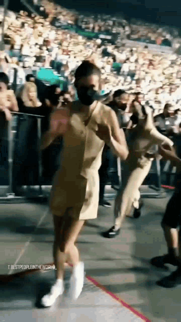 a woman wearing a mask is walking on a stage in front of a crowd of people .