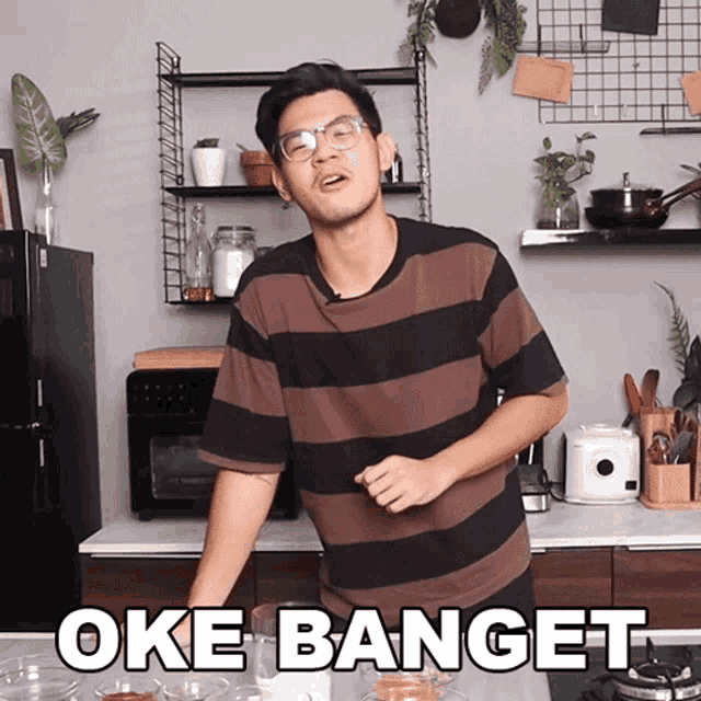 a man in a striped shirt stands in a kitchen with the words oke banget on the bottom