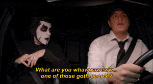 a man in a white shirt and tie is talking to a woman in a black mask in a car