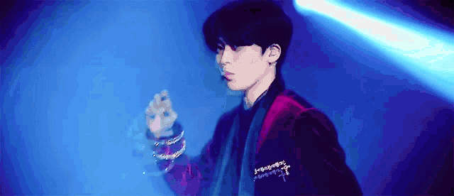 a young man in a red jacket is standing in front of a blue light and holding a microphone .