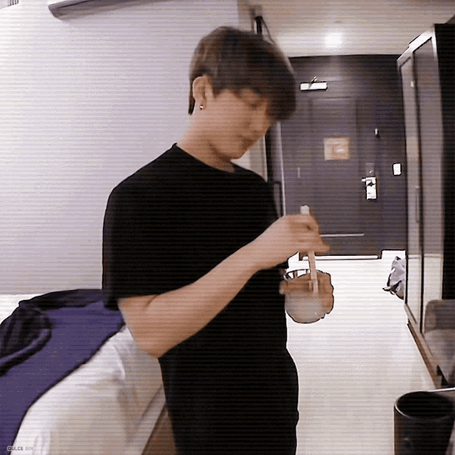 a man in a black shirt is standing in a hotel room holding a bowl of food with chopsticks