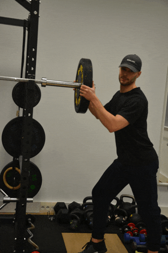 a man lifting a barbell in a gym wearing a black hat that says ' brooklyn athletics ' on it