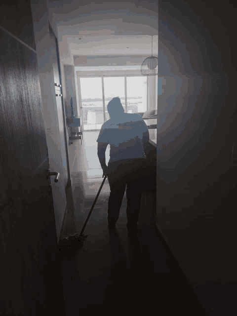 a man cleaning a hallway with a mop and wearing a shirt that says ' cleaner ' on it