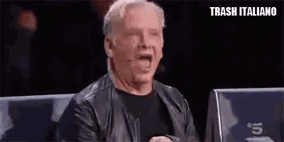 a man in a leather jacket is sitting in front of a microphone and making a funny face .