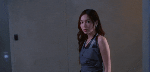 a woman in a gray dress and earrings looks at the camera