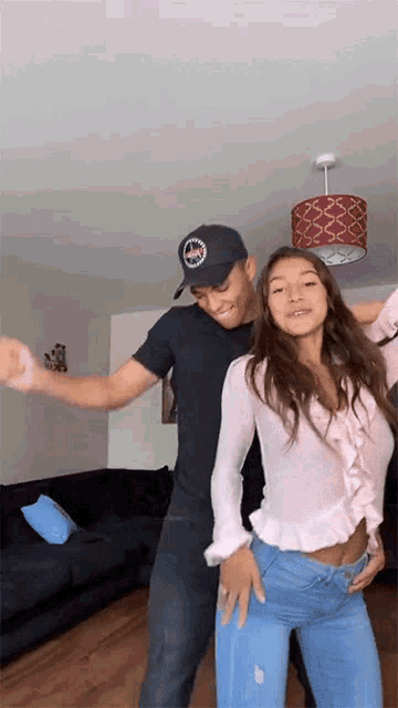 a man and a woman are dancing in a living room and the man is wearing a hat that says abercrombie