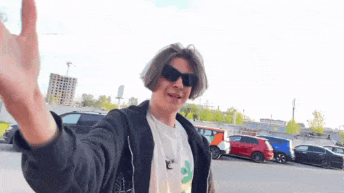 a young man wearing sunglasses and a t-shirt is standing in front of a parking lot .
