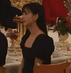 a woman in a black dress is sitting in a chair at a table .