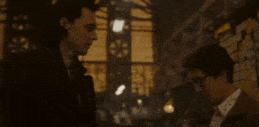 two men are standing next to each other in a dark room and looking at each other .