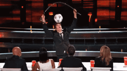 a man in a suit and tie is juggling a soccer ball with a stick