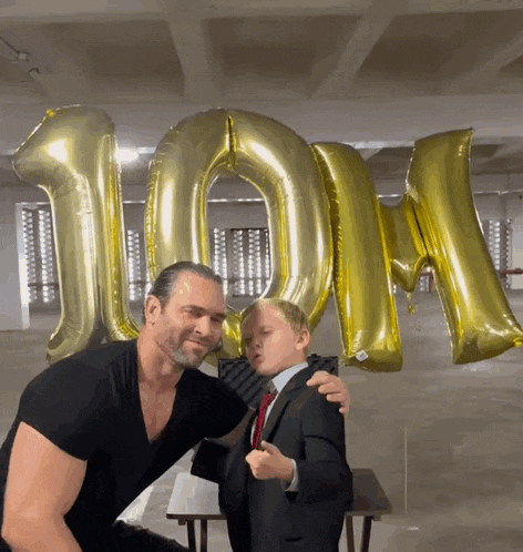 a man and a boy are posing for a picture in front of balloons that say 100m