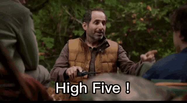 a man in a vest is holding a screwdriver and says high five !