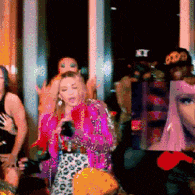 a woman in a pink jacket is singing into a microphone in front of a group of women .