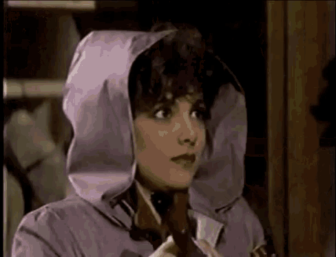 a woman is wearing a purple jacket with a hood and holding a cigarette .