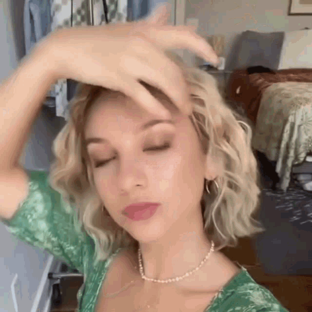 a woman in a green dress is touching her hair while wearing a necklace .