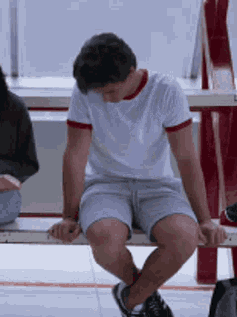 a man in shorts sits on a bench with his head down