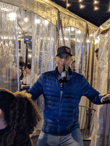 a man in a blue jacket is drinking a bottle of beer