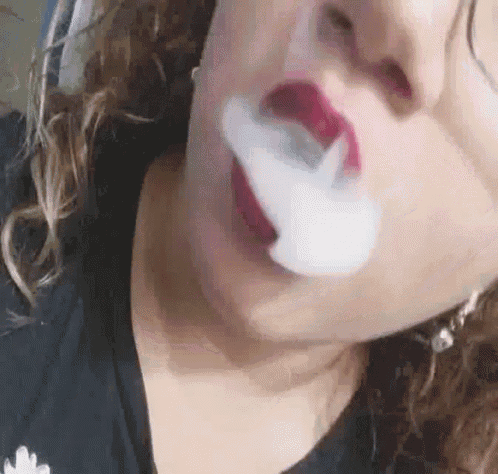 a woman is blowing smoke out of her mouth while wearing red lipstick .