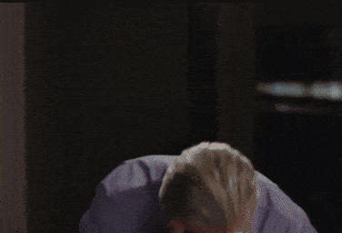 a man with gray hair is sitting in a dark room with his head on a pillow .