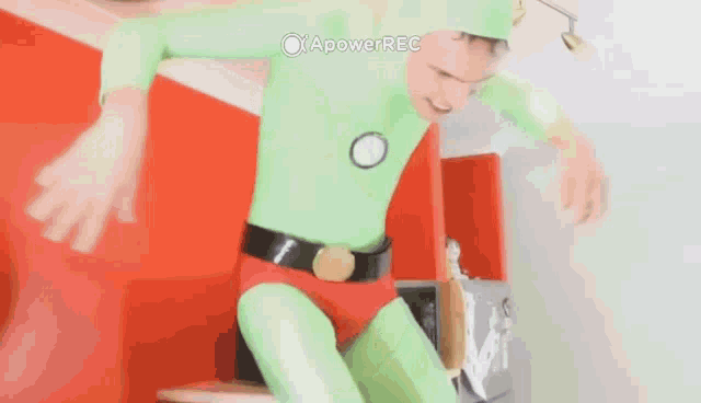 a person in a green superhero costume is standing in front of a red wall .