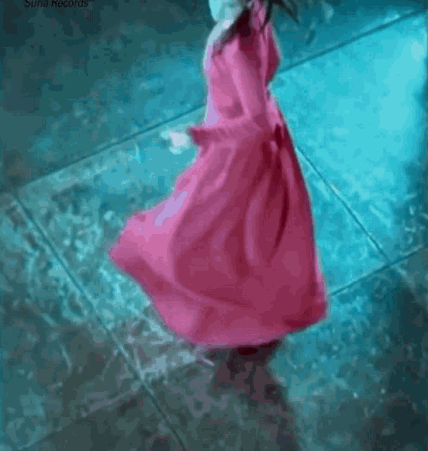 a woman in a long pink dress is dancing on a blue floor