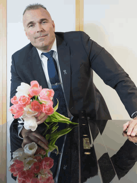 a man in a suit and tie holds a bouquet of pink and white tulips