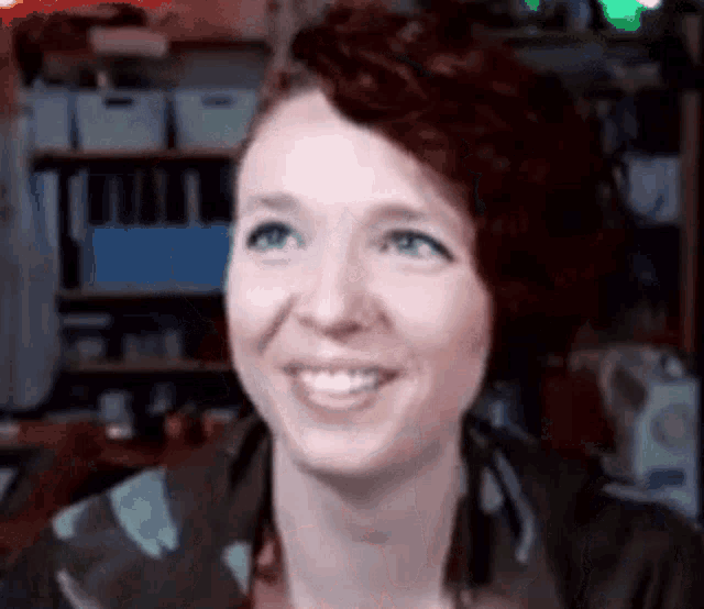 a woman with red hair and blue eyes is smiling in front of a shelf .