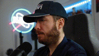 a man with a beard is sitting in front of a microphone wearing a hat .
