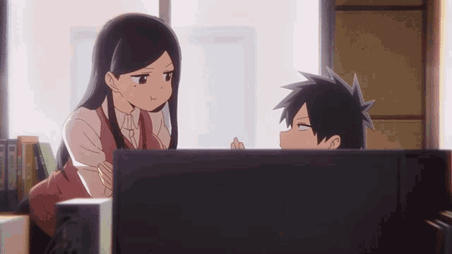 a girl and a boy are looking at a computer monitor