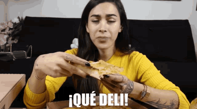 a woman in a yellow sweater is eating a slice of pizza with the words ique deli written on the bottom