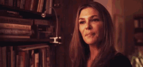 a woman is smiling while standing in front of a bookshelf .