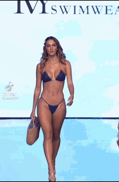 a woman in a bikini is walking down the runway at a swimsuit show .