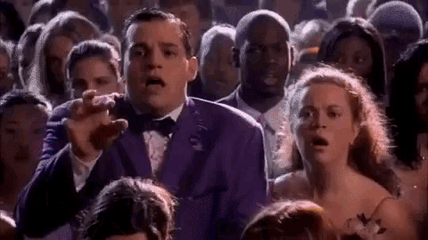 a man in a purple tuxedo is standing in a crowd of people .