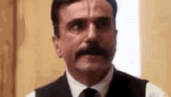 a man with a mustache is wearing a suit and tie and making a funny face .