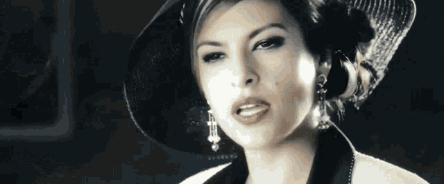 a woman wearing a black hat and earrings is looking at the camera