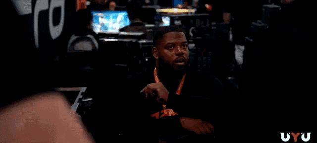 a man with a lanyard around his neck is sitting in a dark room with the letters uyu on the bottom