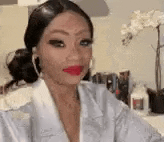 a woman wearing a white robe and red lipstick is sitting in front of a table .