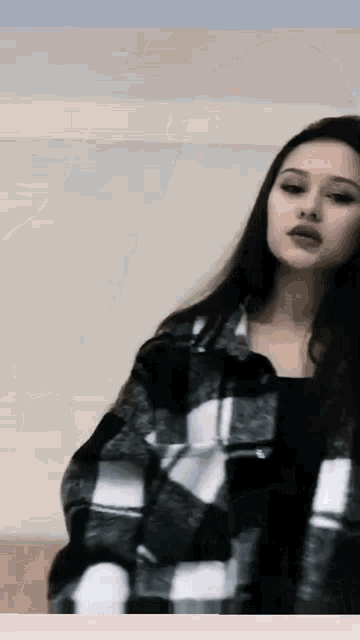 a young woman wearing a plaid jacket is standing in front of a wall .