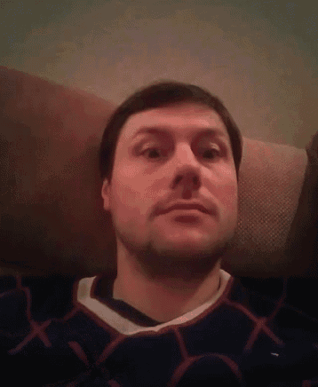 a man with a beard is laying on a couch and taking a selfie